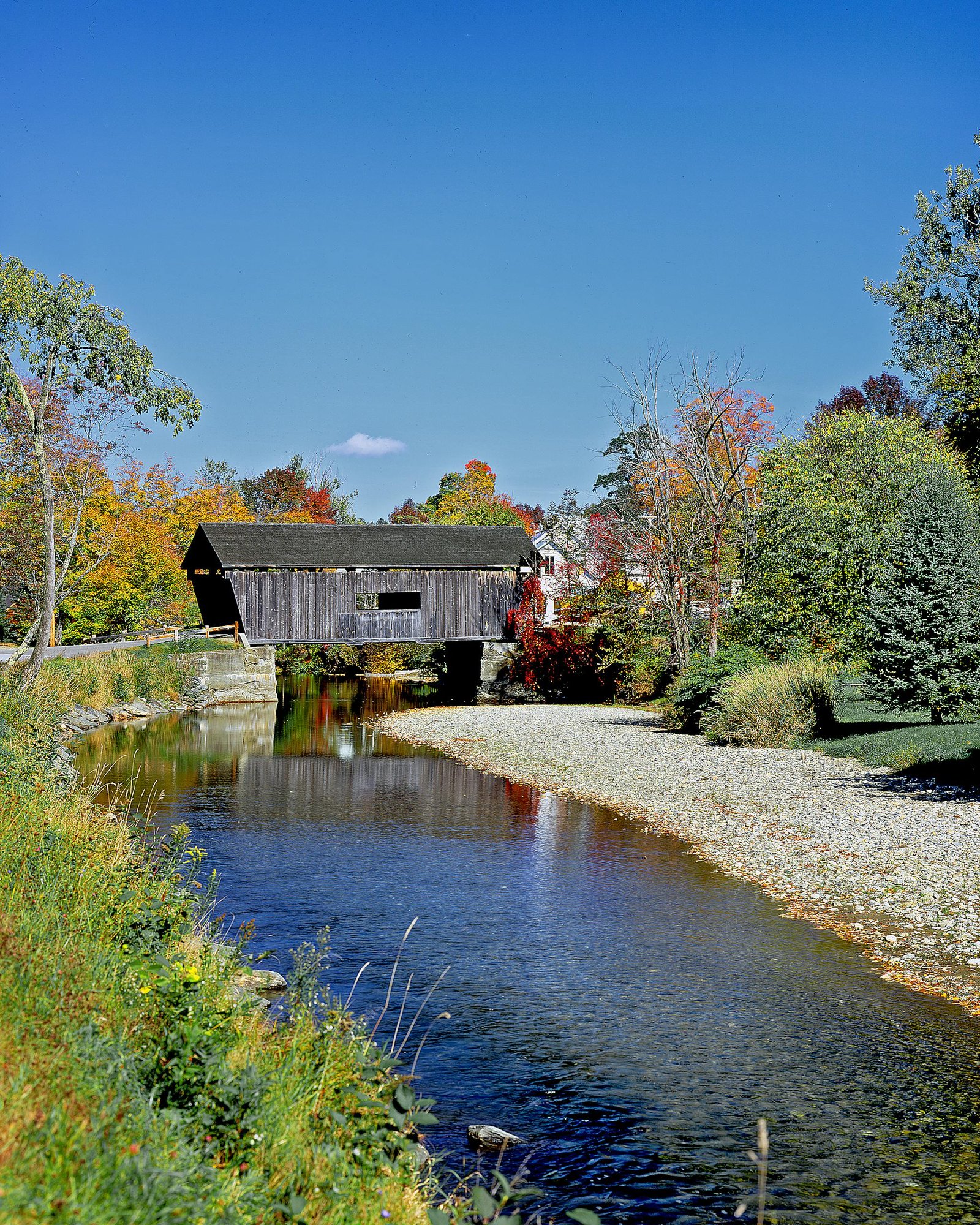Picturesque autumn view of a covered bridge over a stream in Warren, Vermont.