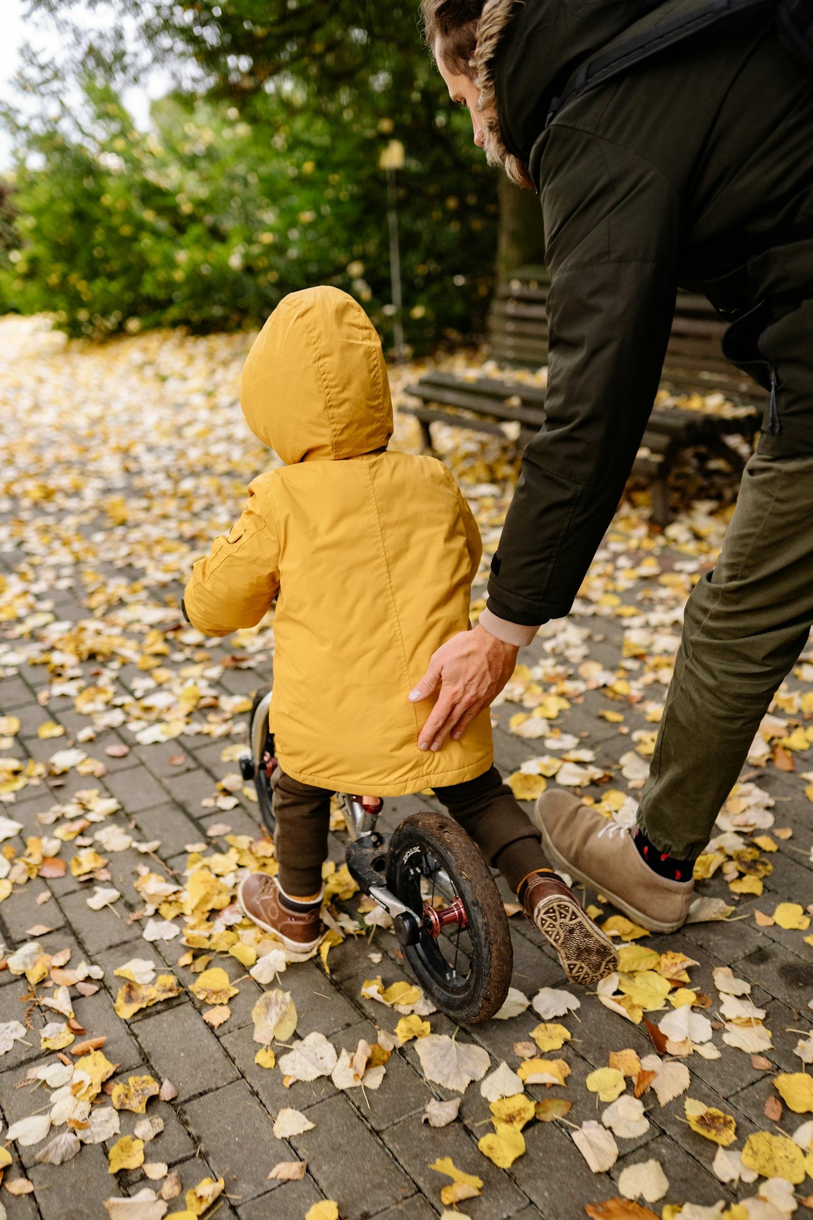 A father and son enjoy a playful autumn day as they ride a bicycle in the park.
