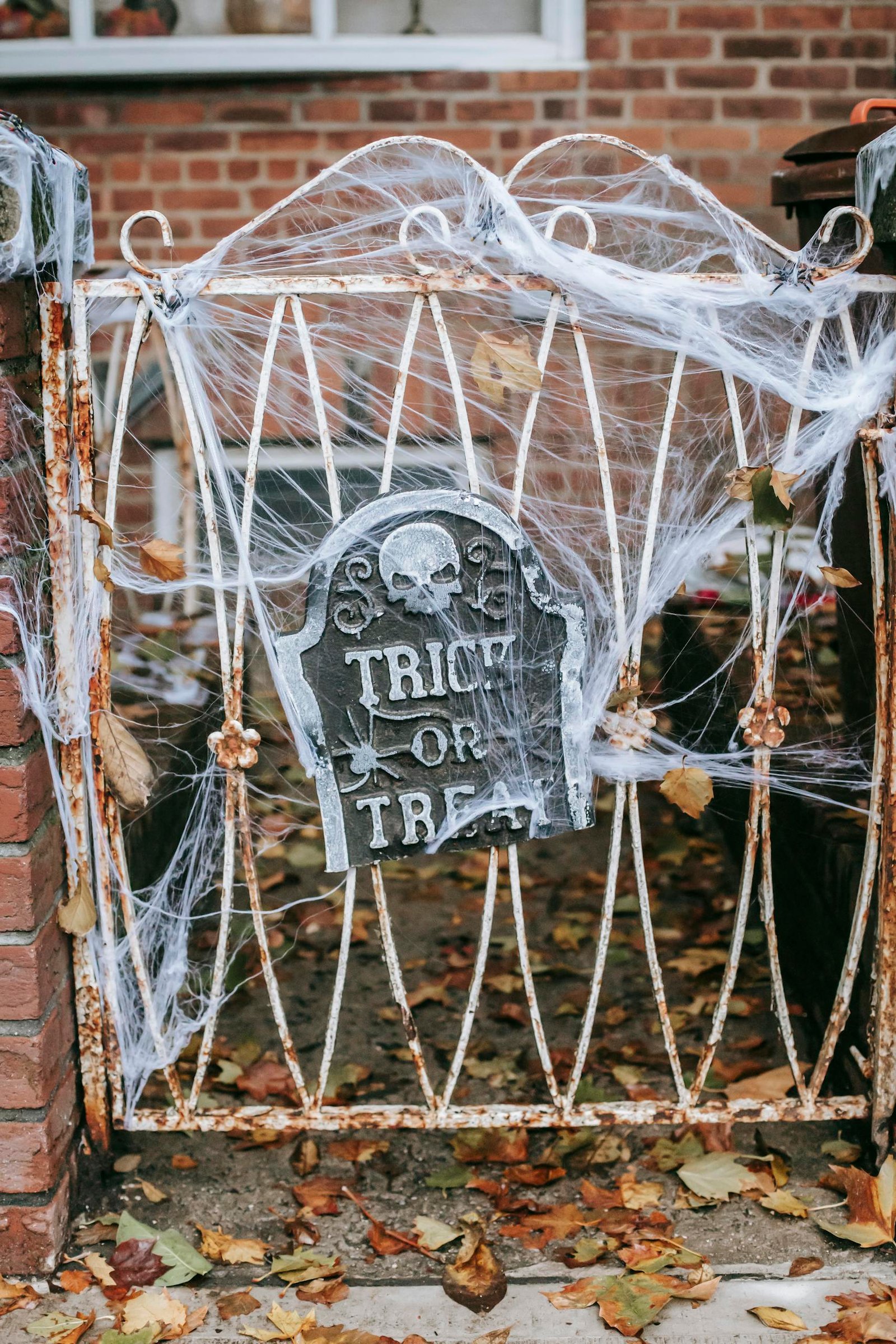 Rusted gate with Halloween decor and 'Trick or Treat' sign surrounded by autumn leaves.