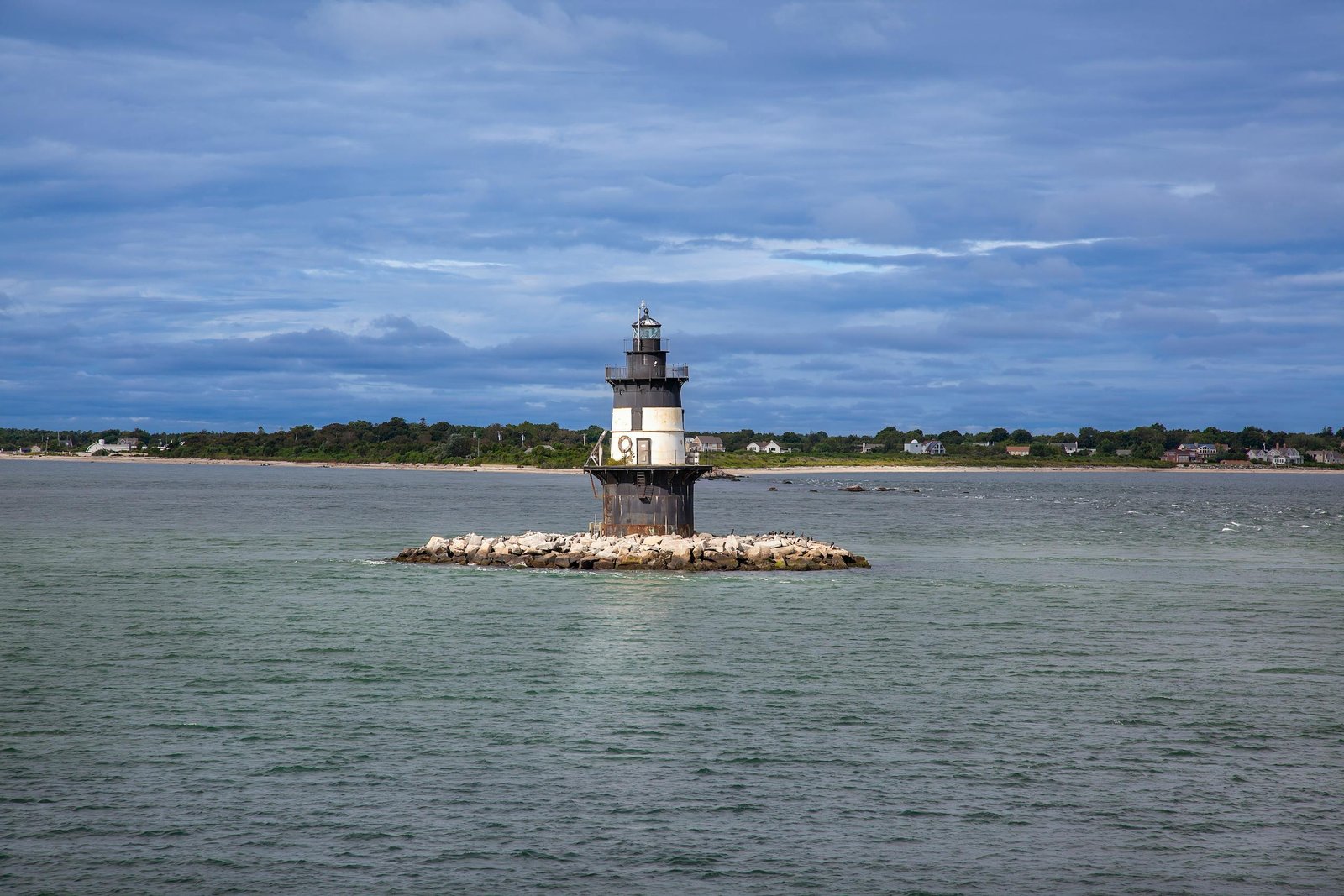 Serene view of Orient Point Lighthouse on a rocky islet in New York, surrounded by calm sea and distant shoreline.