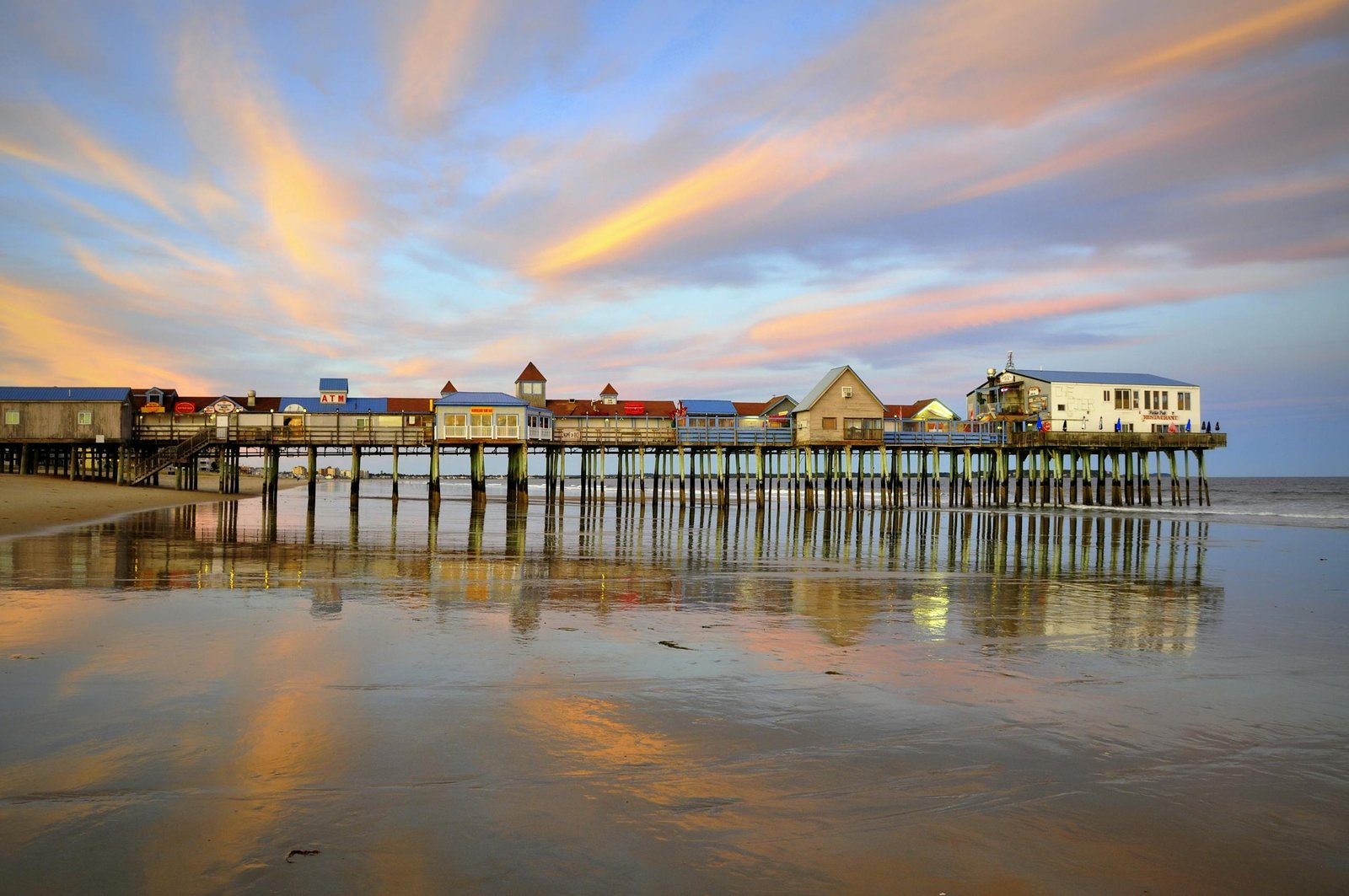 Beautiful sunset over Old Orchard Beach pier with colorful sky reflections.