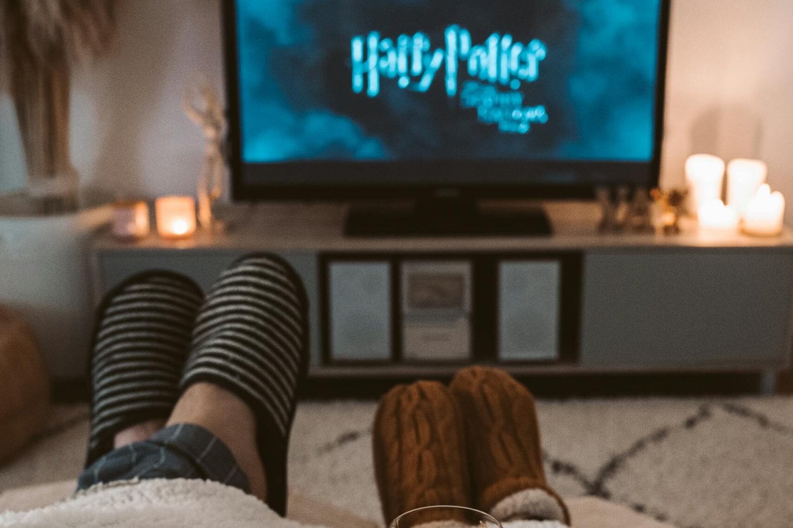A couple enjoys a cozy movie night with drinks, wrapped in blankets, watching a Harry Potter film on TV.