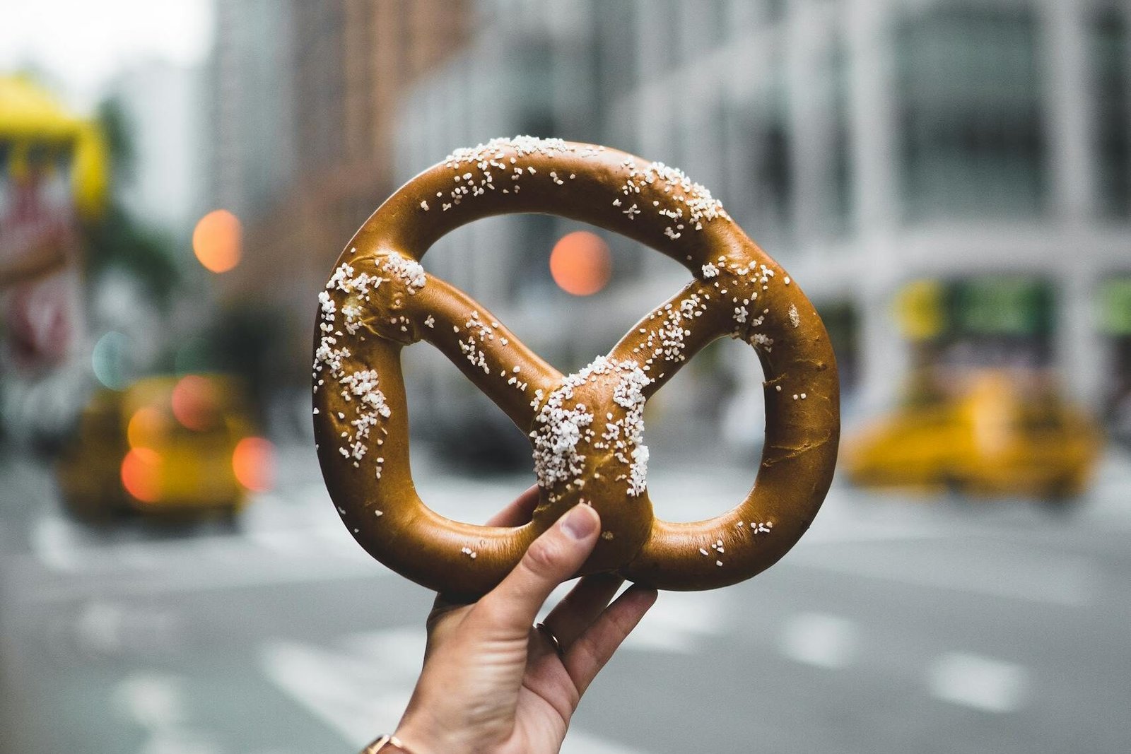 Close-up of a hand holding a salted pretzel against a bustling New York City street backdrop.